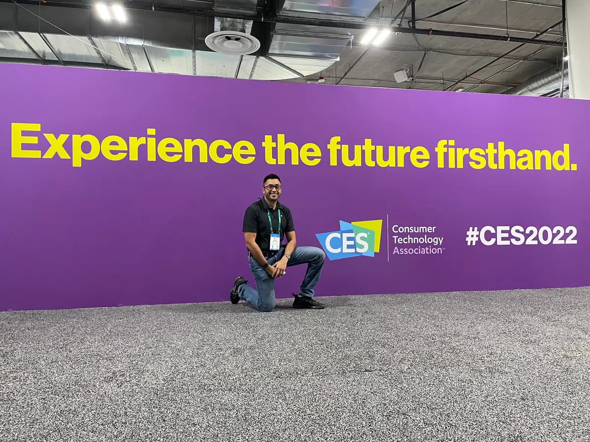 A person kneeling in front of a CES 2022 banner reading Experience the future firsthand